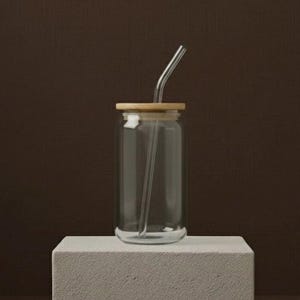 Peut inclure: Un verre &agrave; boire transparent en forme de canette avec un couvercle en bambou et une paille en verre transparent. Le verre repose sur un bloc rectangulaire blanc sur fond marron. La paille est courb&eacute;e en haut.