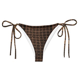 May include: Brown bikini bottom with a repeating pattern of small, dark circles. The bikini bottom has white lining and brown tie strings on each side. The overall design is a neutral color palette.