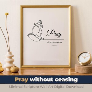 May include: A framed print with the words "Pray without ceasing" and an illustration of praying hands. The artwork is in a gold frame and sits on a wooden surface with decorative vases and a clock.
