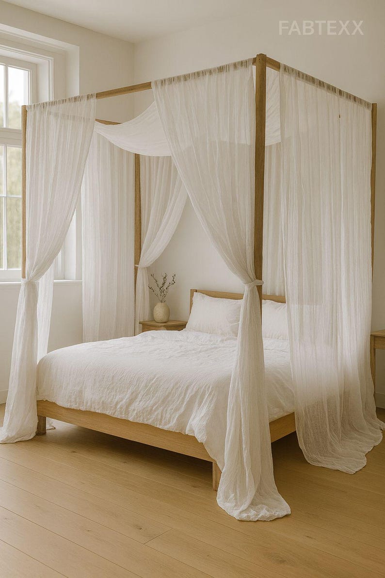 May include: A wooden four-poster bed with white bedding and sheer white curtains. The bed frame is light-colored wood, and the curtains are draped around the frame. The room has a neutral color palette with a wooden floor.