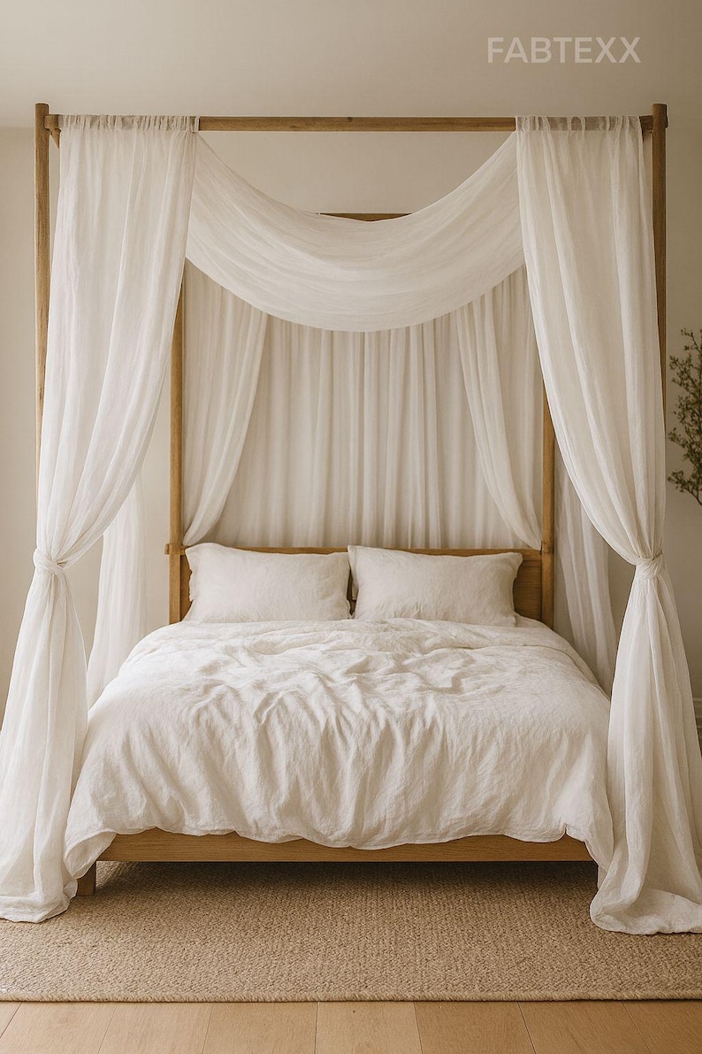 May include: A wooden four-poster bed draped with white sheer curtains. The bed is made with white linens and pillows. The room has a neutral color palette, with a beige rug and light-colored walls. The brand name FABTEXX is visible in the top right corner.