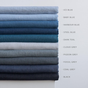 May include: A stack of folded linen fabric samples in various shades of blue and gray. Colors include Ice Blue, Baby Blue, Harbour Blue, Steel Blue, Dark Teal, Cloud Grey, Pigeon Grey, Fossil Grey, Coal Grey, and Black. The names of the colors are listed next to each fabric.