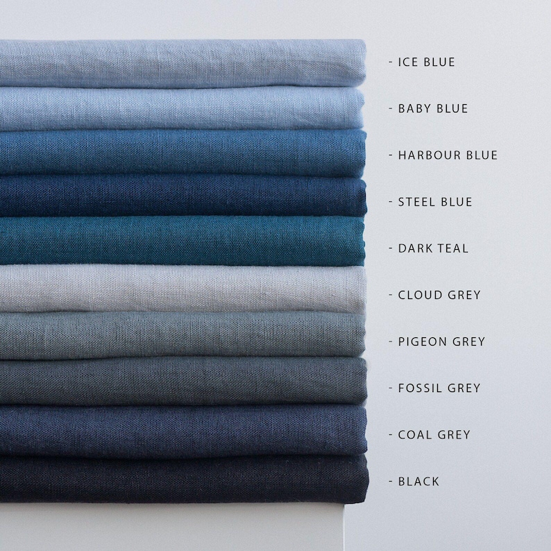 May include: A stack of folded linen fabric samples in various shades of blue and gray. Colors include Ice Blue, Baby Blue, Harbour Blue, Steel Blue, Dark Teal, Cloud Grey, Pigeon Grey, Fossil Grey, Coal Grey, and Black. The names of the colors are listed next to each fabric.