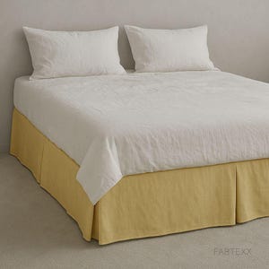 May include: A bed dressed with white bedding and two pillows. The bed skirt is a solid yellow colour. The bed is set against a neutral-coloured wall and floor. The brand name "FABTEXX" is visible on the bed skirt.