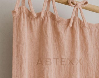 May include: A dusty rose-colored linen curtain with tie-top details. The curtain hangs from a wooden rod, with the text "ABTEXX" subtly visible on the fabric. The fabric has a textured appearance.