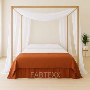 May include: A four-poster bed with a light wood frame, draped with white fabric and a rust-coloured bedspread. The bed is made up with white sheets and a matching rust-coloured bed skirt. The text "FABTEXX" is visible on the bed skirt.