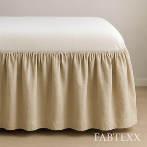 Może przedstawiać: Łóżko z beżową spódnicą do łóżka. Spódnica łóżka jest marszczona u góry i zwisa do podłogi. Spódnica łóżka jest wykonana z miękkiej, teksturowanej tkaniny. Łóżko jest przykryte kremową prześcieradłem.