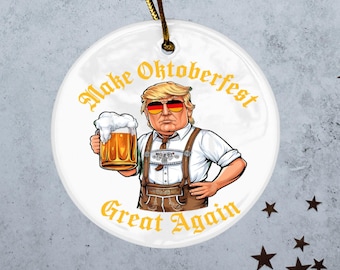 May include: White ceramic ornament featuring a cartoon illustration of a person in sunglasses and German attire, holding a beer stein. The text "Make Oktoberfest Great Again" is in gold lettering.