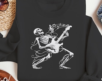 Peut inclure: Sweat-shirt noir avec une illustration blanche d'un squelette jouant de la guitare électrique. Des notes de musique flottent au-dessus de la guitare. Le squelette est dans une pose dynamique. Le design est détaillé et artistique.