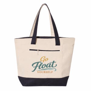 Peut inclure: Un sac fourre-tout en toile couleur crème avec des anses et une base noires. L'avant présente une poche zippée et le texte "Go Float YOURSELF" imprimé dans une police stylisée aux couleurs or et sarcelle. Le sac a une ouverture large.