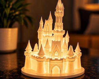 May include: A white, three-dimensional printed castle lamp featuring multiple towers, pointed spires, and arched entryways. The structure is illuminated from within, casting a warm, soft glow through the translucent material onto the circular base.