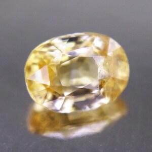 May include: A faceted oval-shaped yellow gemstone with a transparent appearance and multiple geometric cuts that reflect light. The stone displays a vibrant golden hue with internal clarity and sharp edges, showcasing a polished surface finish.