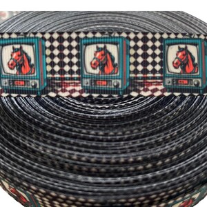 May include: A roll of black and white patterned ribbon. The ribbon features a repeating pattern of retro televisions with a red horse head inside. The background has a black and white checkered pattern.