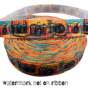 May include: A roll of colorful ribbon featuring a repeating pattern of vintage cameras in various colors. The ribbon has a vibrant orange, blue, and yellow background. The text "Watermark not on ribbon" is at the bottom.