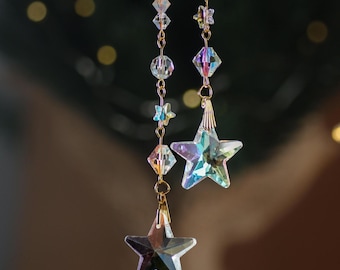May include: Two iridescent crystal star shaped charms hang from gold chains with clear crystal beads.