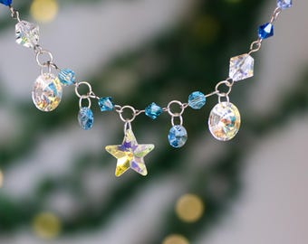 May include: A silver chain necklace with blue and clear crystal beads and a star-shaped pendant. The necklace has a variety of crystal shapes, including round, square, and star-shaped.