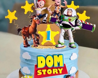 Peut inclure: Un gâteau au glaçage bleu clair décoré de figurines Toy Story incluant Woody, Jessie, Buzz l'Éclair, Pile-Poil, un alien et Monsieur Patate. Le gâteau présente une enseigne centrale avec le chiffre 1 et le texte DOM STORY.