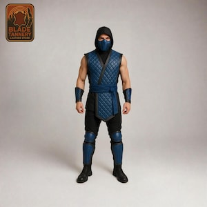 May include: A blue and black costume featuring a quilted vest, arm guards, knee pads, and a face mask. The outfit includes a sash and is worn with black trousers and boots. The image also shows a logo that says "Blade Tannery Leather Store".