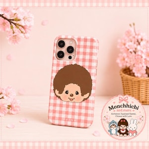 Puede incluir: Una funda para teléfono con patrón de cuadros vichy en rosa y blanco y una ilustración de un personaje de pelo castaño. La funda tiene un recorte para la cámara y el nombre BURGA en la parte inferior. Una pegatina circular muestra el texto Monchhichi and more.