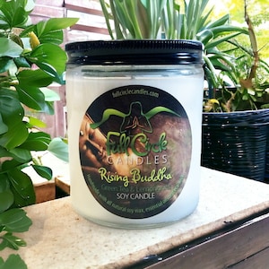 May include: A glass jar candle with a black lid and a label that says "Full Circle Candles Rising Buddha Green Tea & Lemongrass Soy Candle Handmade with all natural soy wax, essential oils and eco-wick."