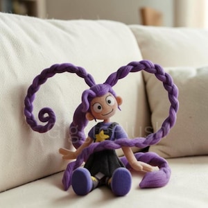 Puede incluir: Mu&ntilde;eca de peluche hecha a mano con cabello morado trenzado. La mu&ntilde;eca viste una camisa morada con una estrella amarilla, una falda negra y zapatos morados. Est&aacute; sentada en un sof&aacute; blanco.