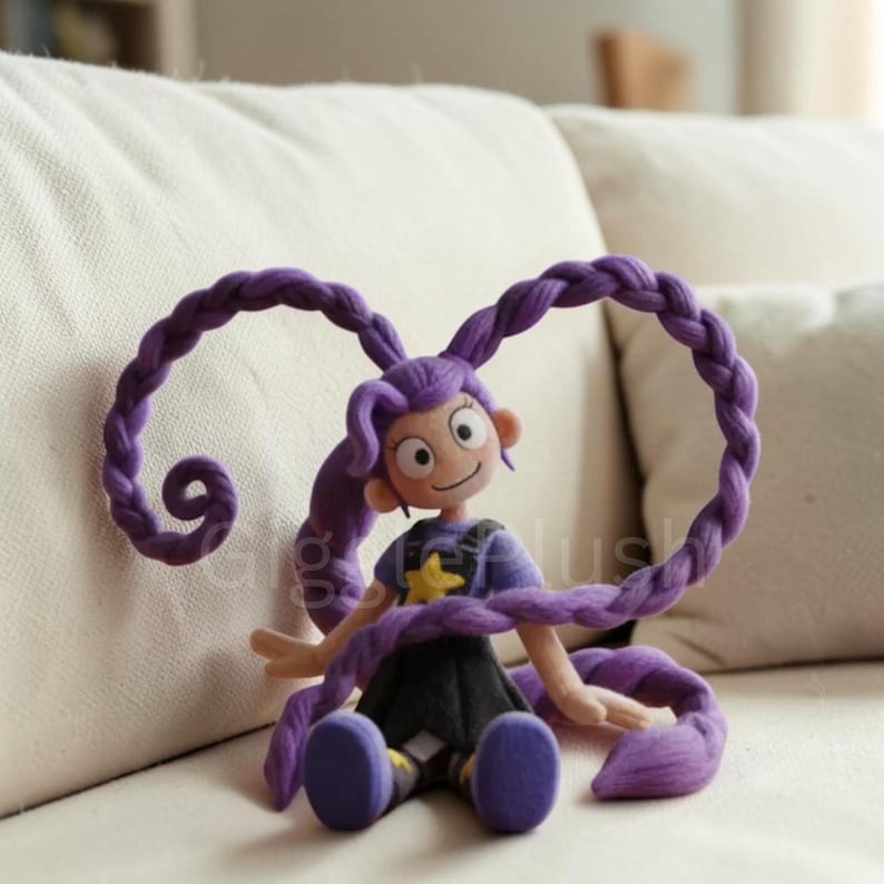 Puede incluir: Mu&ntilde;eca de peluche hecha a mano con cabello morado trenzado. La mu&ntilde;eca viste una camisa morada con una estrella amarilla, una falda negra y zapatos morados. Est&aacute; sentada en un sof&aacute; blanco.