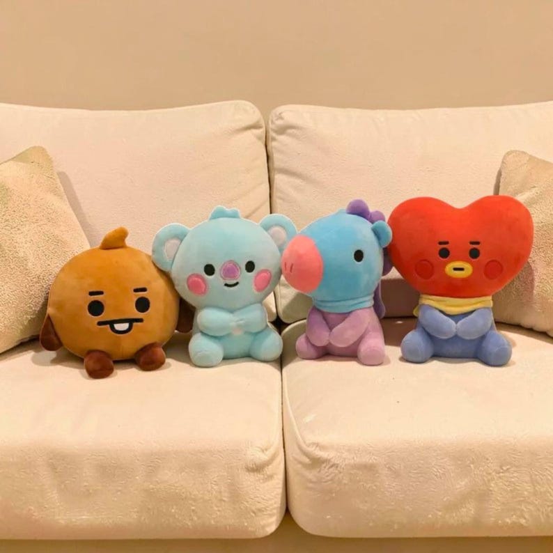 以下が含まれることがあります： 白いソファに座っている、さまざまな色の4つのぬいぐるみキャラクター人形。人形には、丸いオレンジ色のキャラクター、水色のコアラ、青い馬、赤いハート型のキャラクターが含まれています。