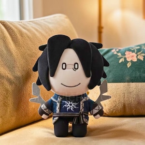 Puede incluir: Muñeco de peluche con cabello negro y una cara sonriente. El muñeco viste una chaqueta azul y blanca estampada con un diseño de sol y pantalones negros. Sostiene dos armas grises estilizadas. El muñeco está sentado en un sofá beige.