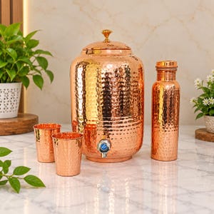 May include: A set of hammered copper drinkware including a large water dispenser with a lid and a spigot, a tall water bottle with a cap, and two matching tumblers. Each piece features a textured, reflective surface with a warm metallic finish.