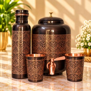 Puede incluir: Un dispensador de agua de metal marrón oscuro con tapa y grifo de color cobre, acompañado de una botella de agua alta a juego y dos vasos. Cada artículo presenta un intrincado patrón floral repetitivo de color cobre en el exterior.