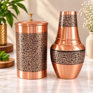 Peut inclure: Un récipient cylindrique en cuivre avec un couvercle et un vase en cuivre assorti, tous deux ornés d'un motif floral sombre et complexe gravé dans le métal. Le récipient possède un petit bouton arrondi couleur laiton sur son couvercle plat.