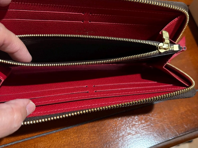 May include: Open, red interior wallet with a brown exterior and a gold zipper. The wallet has multiple card slots and a zippered compartment. The wallet is open, revealing the interior.