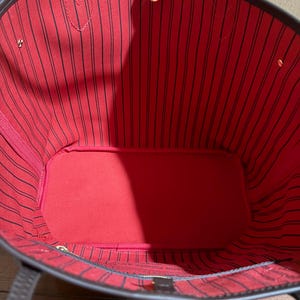 May include: Open view of a brown tote bag with a red interior. The interior features black vertical stripes. The bag has brown handles and gold-colored hardware. The bag's interior has a heart-shaped detail.
