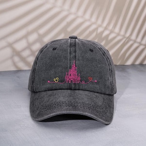 Op de afbeelding: Donkergrijze baseballcap met een roze geborduurd kasteelontwerp, een gele Mickey Mouse-kop en een rood hart. De cap heeft een gebogen klep en een verstelbare band.