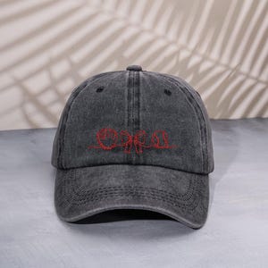 Peut inclure: Casquette de baseball gris anthracite avec une visière incurvée. Le chapeau présente un motif brodé rouge sur le devant. La casquette a une construction classique à six panneaux et une sangle réglable à l'arrière.