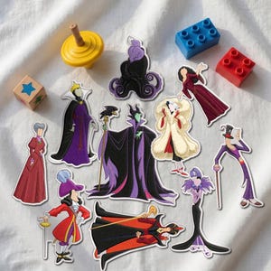 May include: A collection of embroidered patches featuring various animated villain characters in colorful outfits, including purple, red, black, and white designs, accompanied by a yellow spinning top, a wooden block, and two plastic building bricks.