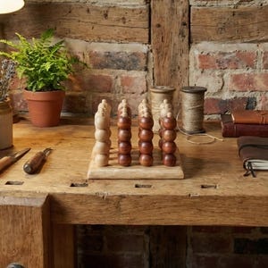 Könnte beinhalten: Ein Holzbrettspiel mit hell- und dunkelbraunen Spielsteinen. Die Spielsteine sind in Reihen auf einer Holzbasis angeordnet. Der Hintergrund umfasst eine Backsteinmauer, eine Topfpflanze und andere Bastelmaterialien.