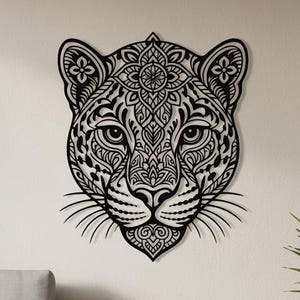 May include: Black metal wall art of a leopard's head with intricate, symmetrical patterns. The artwork features detailed designs within the leopard's face and around its head, creating a striking visual effect. This decorative piece is suitable for home decor.