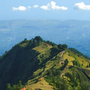 Könnte beinhalten: Luftaufnahme eines Bergkamms mit mehreren Zelten entlang des Weges. Die Zelte haben orangefarbene und blaue Dächer. Der Berg ist mit grünem Gras und Bäumen bedeckt. Der Himmel ist blau mit ein paar weißen Wolken.