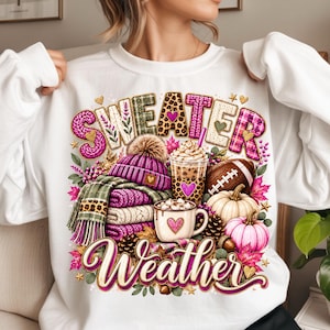 Peut inclure: Un sweat-shirt blanc à col rond avec une impression graphique portant le texte "SWEATER Weather". Le motif comprend une pile de pulls en tricot pliés, un bonnet, une tasse de café, un ballon de football, des citrouilles, des pommes de pin et des feuilles d'automne dans des tons roses et bruns.