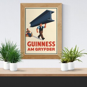 Op de afbeelding: Een ingelijste print met een vintage Guinness-advertentie. De afbeelding toont een man die een grote stalen balk draagt, met een andere man die ernaast zit. De tekst "GUINNESS AM GRYFDER" staat in het rood. De print zit in een houten lijst.