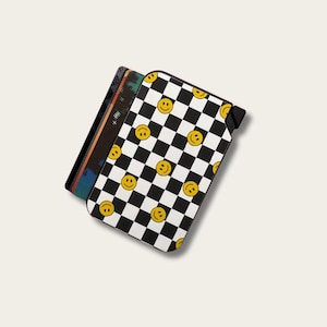 May include: A black and white checkered wallet with yellow smiley faces. The wallet is open, revealing several cards with colorful designs. The wallet has a black strap on the side.
