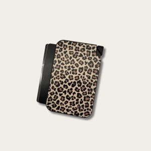 May include: A black and tan leopard print phone case. The case has a black border and a tan background with brown spots. The case is rectangular and appears to be made of a hard material. The phone case is shown on a light background.