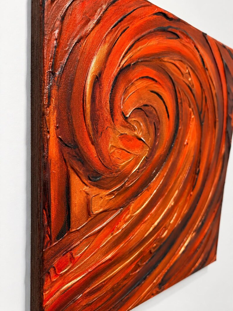 May include: A square canvas painting featuring thick, textured impasto brushstrokes in shades of vibrant orange, deep red, and dark brown. The paint is applied in a swirling, circular motion, creating a dynamic, raised surface.