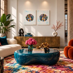 May include: A living room featuring a teal kidney-shaped coffee table, a cream-colored sofa with teal and floral pillows, a rust-colored channel-tufted chair, a black marble side table, and a gold sideboard with two abstract circular paintings.