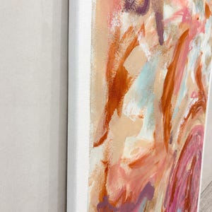 May include: An abstract painting on a rectangular canvas featuring thick, expressive brushstrokes in shades of burnt orange, soft pink, cream, and deep purple. The paint texture is visible across the surface, framed by a clean white border.