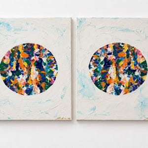 Op de afbeelding: Twee rechthoekige doeken met een centrale cirkel gevuld met dikke, impasto-stijl penseelstreken in levendige tinten blauw, oranje, geel, groen en roze, tegen een getextureerde witte achtergrond met vage blauwe accenten.