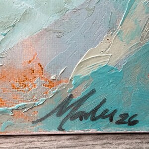 May include: An abstract oil painting on canvas featuring thick, textured impasto brushstrokes in shades of turquoise, cream, and muted orange. The bottom right corner displays a dark, handwritten signature that reads Malu followed by the number 26.