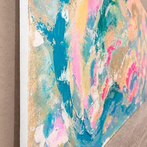 May include: An abstract painting on canvas featuring thick, textured layers of paint in vibrant shades of turquoise, bright pink, soft yellow, and metallic gold. The composition displays swirling, energetic brushstrokes and palette knife marks.