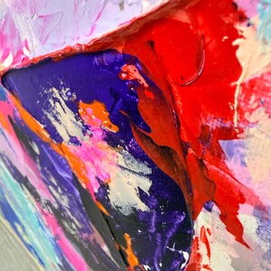 Op de afbeelding: Een abstract schilderij met dikke, getextureerde impasto-lagen olieverf. De compositie toont een levendig palet van dieppaars, felrood, neonroze, oranje en lichtlavendel, met zichtbare penseelstreken en verhoogde verfstructuren op het doek.